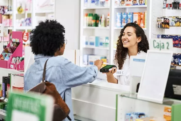 العميل الإناث تقوم بالدفع NFC مع بطاقة الائتمان الخاصة بها في الصيدلية. يبتسم أمين الصندوق القارئ لبطاقة الائتمان في متجر الأدوية.