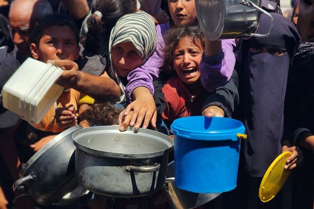 الفلسطينيون الذين يكافحون مع الحشد من الجوع حولها كقوة خيرية يوزع الطعام في منطقة ماواسي في خان يونيس ، غزة 