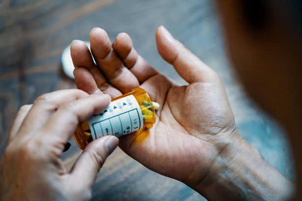 عن قرب من يد الذكور تحمل زجاجة حبوب منع الحمل التي تصب دواء في يده في منزله
