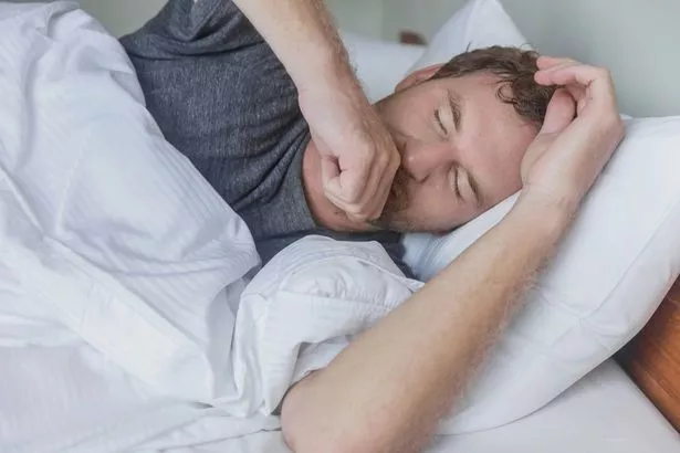 صورة لرجل دويتش شاب مريض يغطي سعاله وهو مستلقي على السرير يحاول النوم