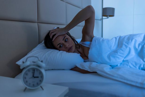 امرأة شابة جميلة في المنزل غرفة نوم مستلقية في السرير في وقت متأخر من الليل في محاولة للنوم معاناة الاضطراب في النوم أو خائفة على كوابيس تبدو حزينة ومجهدة