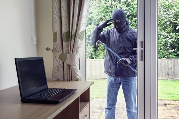 سارق اقتحام منزل عبر نافذة أبواب الفناء مع مربع لسرقة كمبيوتر محمول من مكتب مكتب