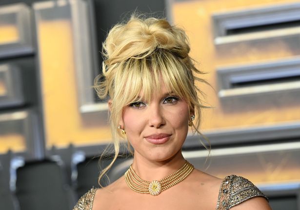 ميلي بوبي براون في ثوب ذهبي وقلادة على سجادة حمراء في فبراير 2025.