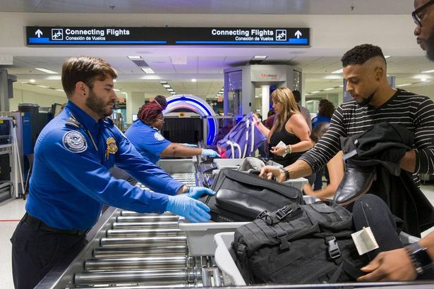 يساعد وكلاء إدارة أمن النقل (TSA) المسافرين على وضع حقائبهم من خلال الماسح الضوئي ثلاثي الأبعاد في مطار ميامي الدولي في 21 مايو 2019 في ميامي ، فلوريدا.