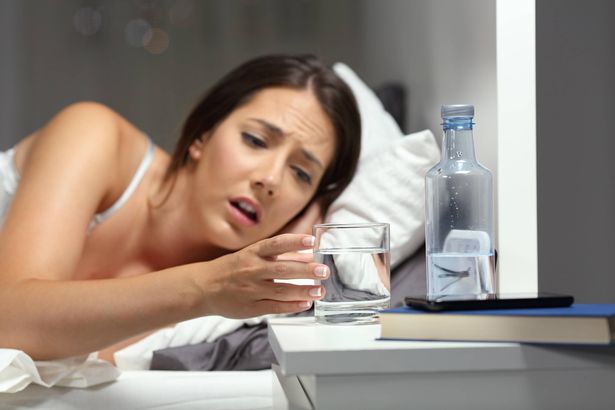 هذه صورة لامرأة مجففة في السرير تصل إلى كوب من الماء. انظر PA ميزة تحذير الجفاف الصحي: يجب استخدام هذه الصورة فقط لمرافقة PA ميزة الجفاف الصحية.