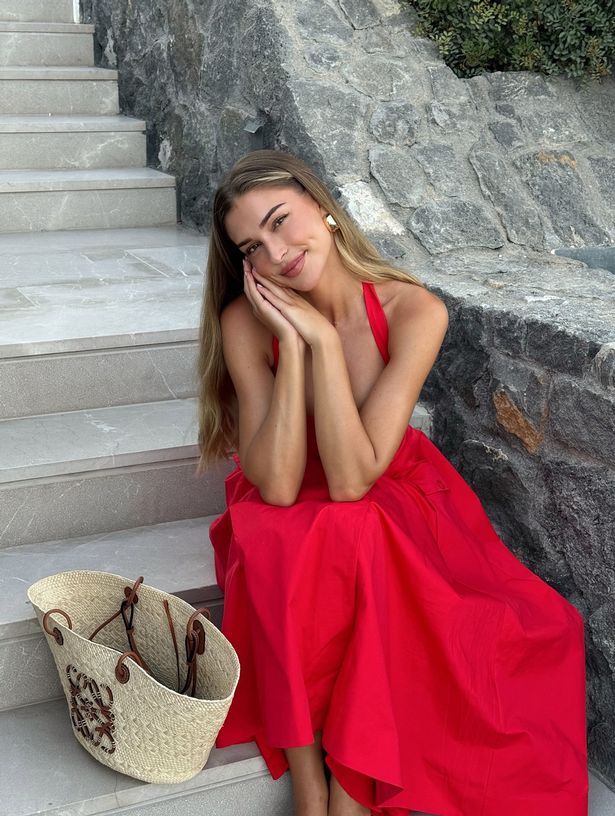 جلست Zara McDermott في فستان أحمر على بعض الخطوات مع حقيبة بجانبها.