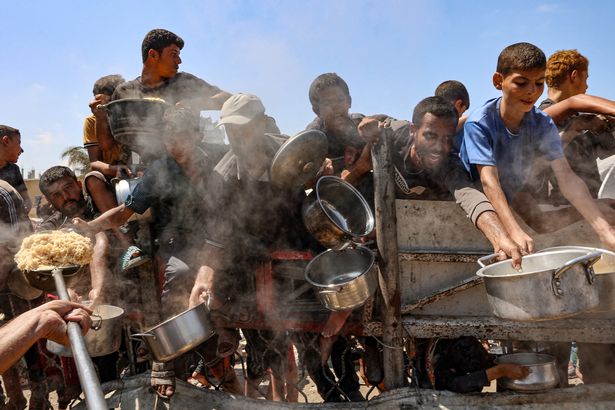 يوسع الرجال والفتيان الفلسطينيون أوانيهم لتلقي الأرز المطبوخ من المطبخ الخيري في مدينة غزة في 23 أغسطس 2025.