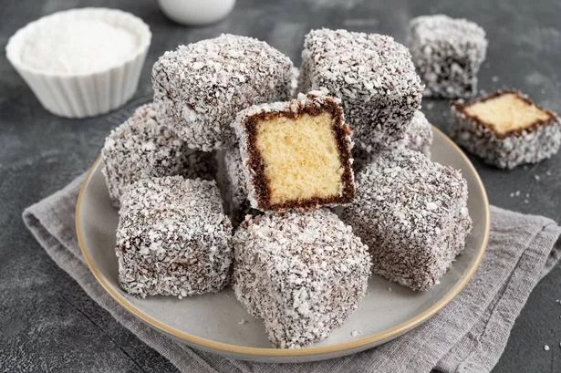 كعكة Lamington الأسترالية التقليدية في الصقيل الشوكولاتة ورقائق جوز الهند على طبق على خلفية خرسانية رمادية مع كوب من الشاي. التركيز الانتقائي