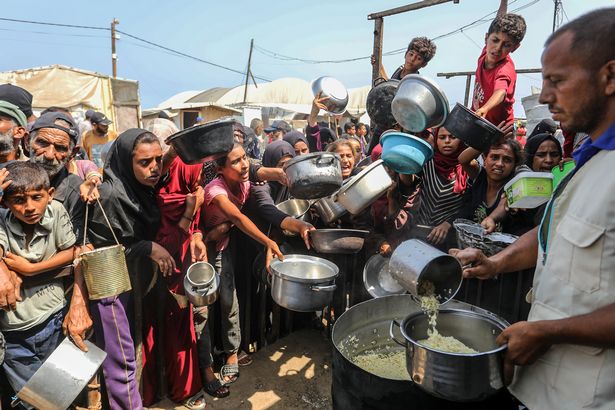 ينتظر الفلسطينيون مع الأواني في أيديهم حيث يوزع منظمة خيرية الطعام على الفلسطينيين الذين يعانون من أزمة طعام تحت الحصار الإسرائيلي في منطقة ماواسي ، خان يونيس ، غزة