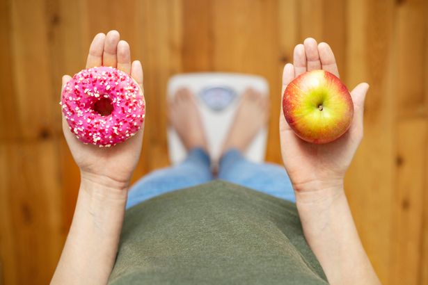 اتباع نظام غذائي شابة تقيس جسم وزنه على مقياس الوزن ، ويمسك بالدونات الحلو والتفاح الأحمر