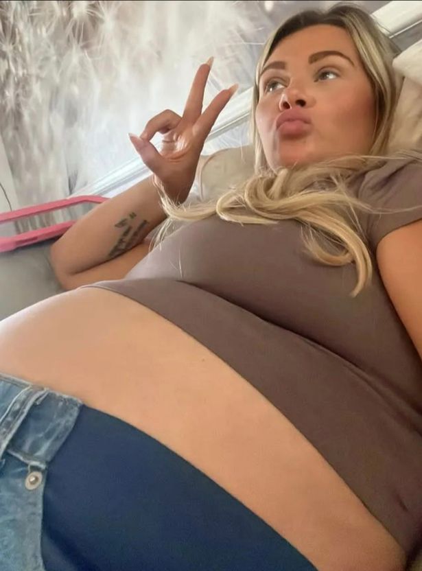 Shaughna Phillips تظهر عثرة طفلها في قمة بنية وبنطلون جينز.