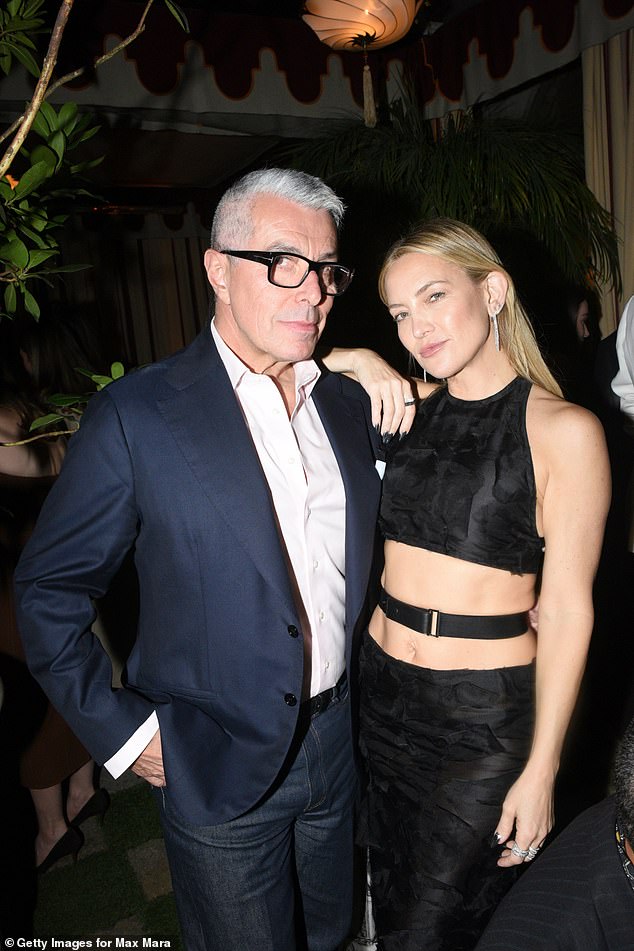 تعاونت كيت مع بلوزة قصيرة سوداء عالية الرقبة مع تنورة متطابقة بطول كامل وحزام ملتوي ملفوف حول خصرها العاري (في الصورة مع جورجيو غيدوتي)