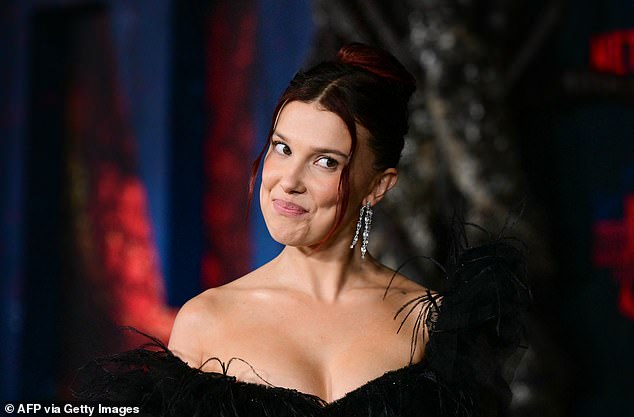 لقد أكملت الزي الشفاف الكاشف بشعرها المصبوغ باللون الأحمر، والذي تم تصفيفه على شكل كعكة مع خيوط مجعدة دقيقة متدلية لتأطير وجهها المرتب بشكل لا تشوبه شائبة.