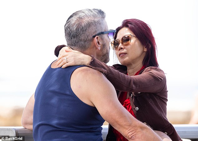 تبادل الزوجان قبلة عاطفية على مقعد في حديقة على الشاطئ، غافلين عن المتفرجين