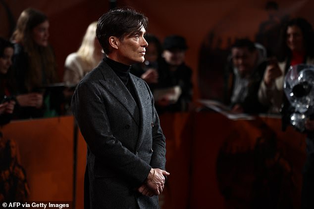 اختار الممثل بدلة رمادية حادة وياقة بولو سوداء أثناء وقوفه على السجادة السوداء