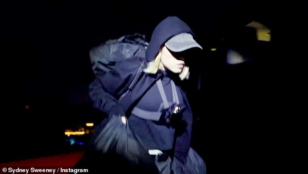 سيدني، التي ترتدي ملابس سوداء بالكامل، تقود الطريق بينما تتسلق المجموعة السياج المحيط بثمانية أقدام وتتسلق التل إلى اللافتة