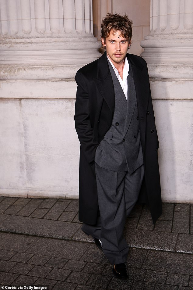 قطع أوستن بتلر شخصية وسيم ببدلة رمادية كبيرة الحجم ومعطف أسود من المصمم