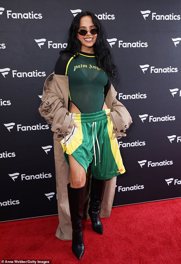 ظهرت الفائزة بجائزة جرامي اللاتينية - التي ستبلغ 29 عامًا الشهر المقبل - حمالة صدرها تحت بدلة شفافة من Palm Angels، وشورت كرة السلة باللونين الأخضر والأصفر، وأحذية سوداء عالية الركبة ومعطف واقٍ من المطر اختاره المصمم مورغان هاروود.