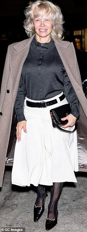 قامت بدس الجزء العلوي في تنورتها ذات الثنيات الناعمة ذات اللون الأبيض العاجي، ووضعت معطفها بشكل عصري على كتفيها وتوازنت بخبرة على زوج من الأحذية ذات الكعب العالي.